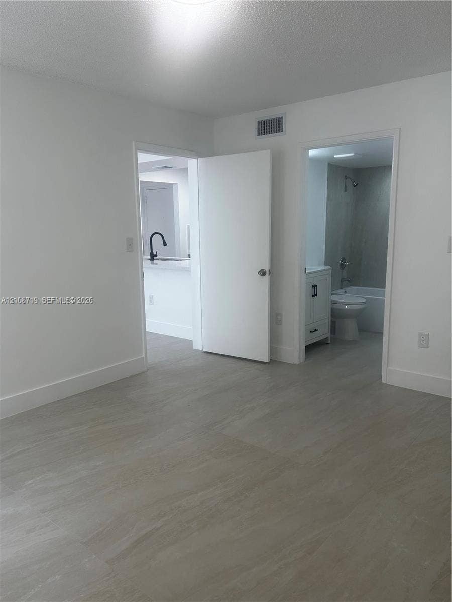 7035 NW 186th Street, #D309, Hialeah, Hialeah, FL 33015 Neutral-toned tile flooring, white-painted interior doors, a bathroom featuring a vanity with shaker-style cabinetry, and a kitchen area highlighting a high-arc matte black faucet
