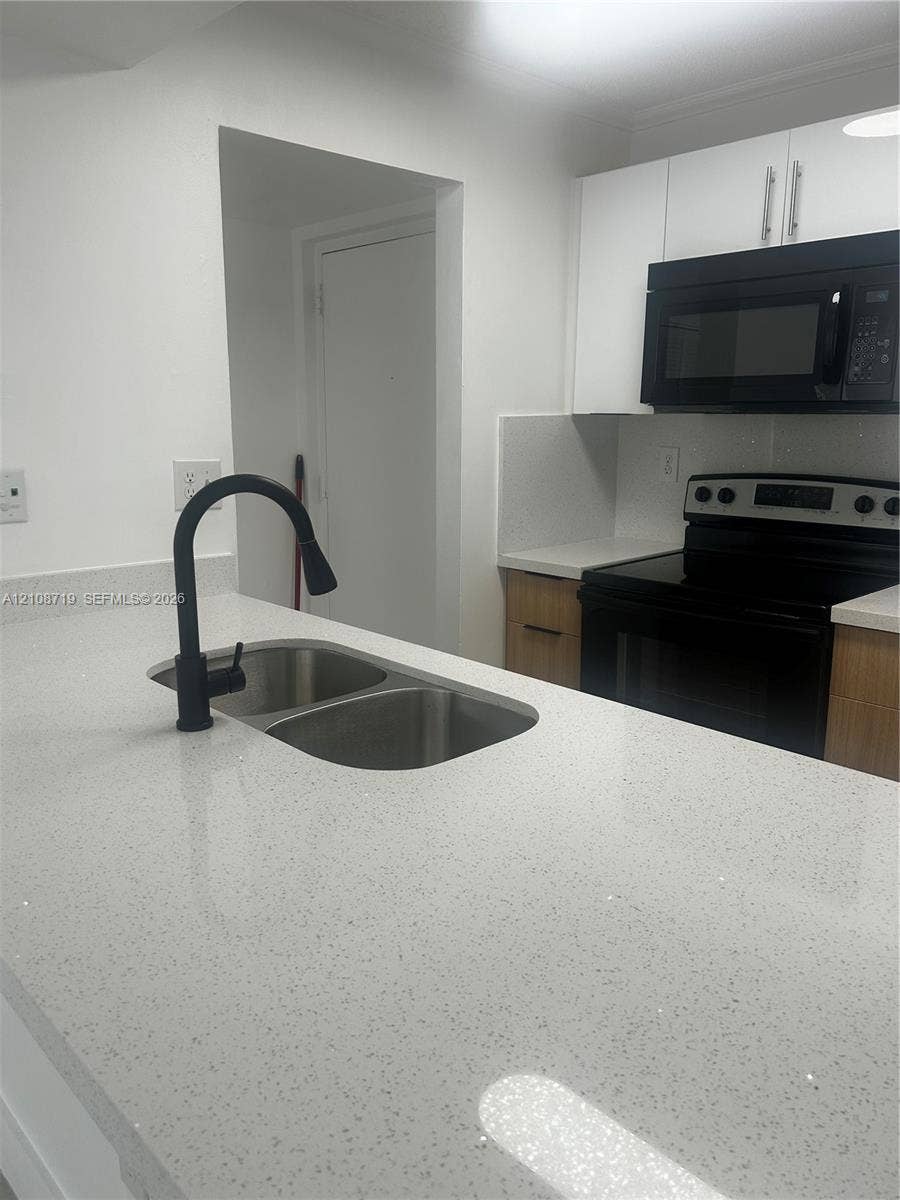 7035 NW 186th Street, #D309, Hialeah, Hialeah, FL 33015 Kitchen featuring a stone-composite countertop, dual-basin stainless steel sink with a matte black pull-down faucet, flat-panel wood-tone cabinetry, and black appliances