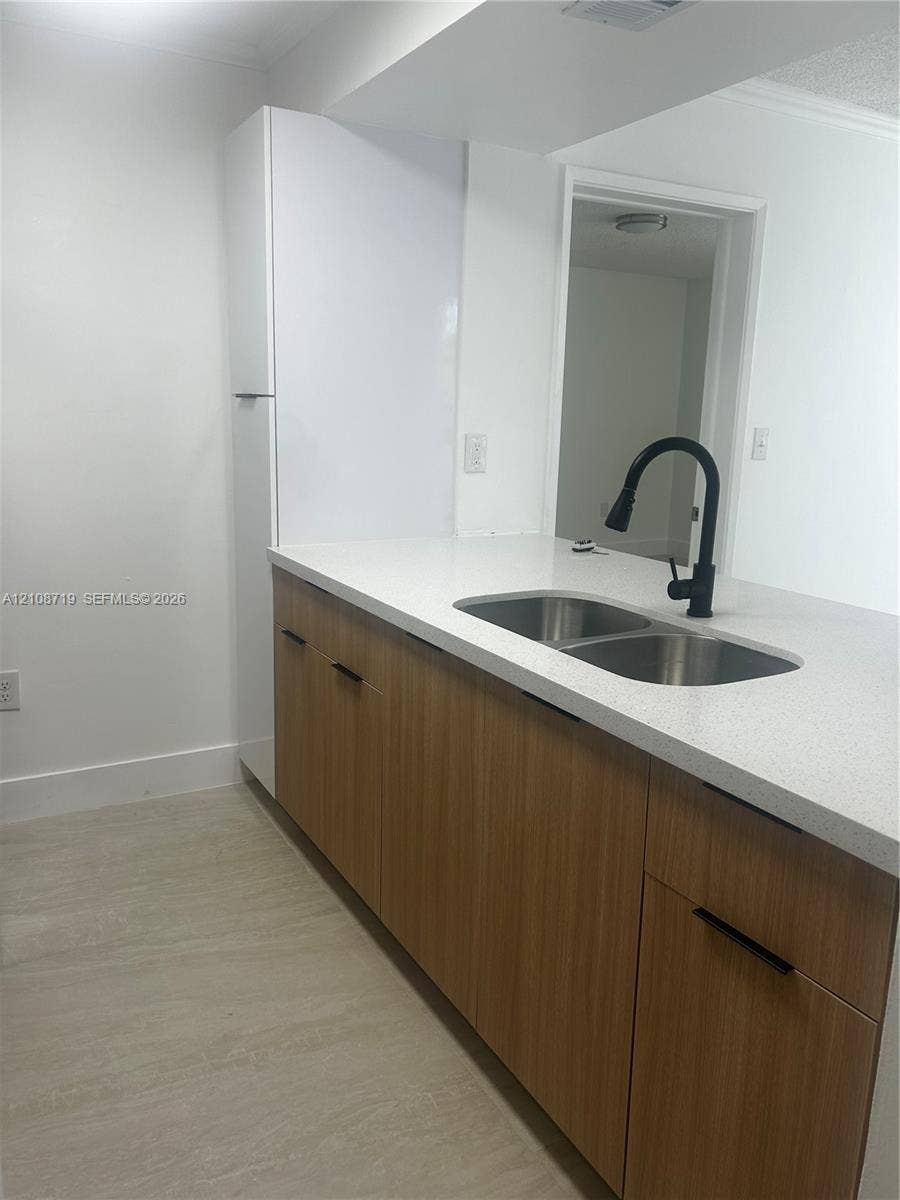 7035 NW 186th Street, #D309, Hialeah, Hialeah, FL 33015 Kitchen featuring wood-finish cabinetry, white stone-surface countertops, a stainless steel dual-basin undermount sink, and a matte black gooseneck faucet