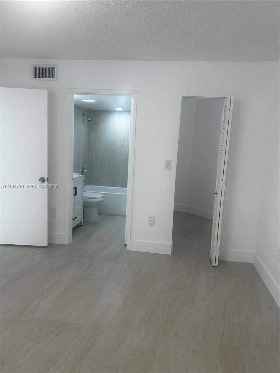 7035 NW 186th Street, #D309, Hialeah, Hialeah, FL 33015 Neutral-toned wood-finish flooring, two interior doorways featuring a closet and a bathroom with a shower-tub combination, and a white vanity with hardware