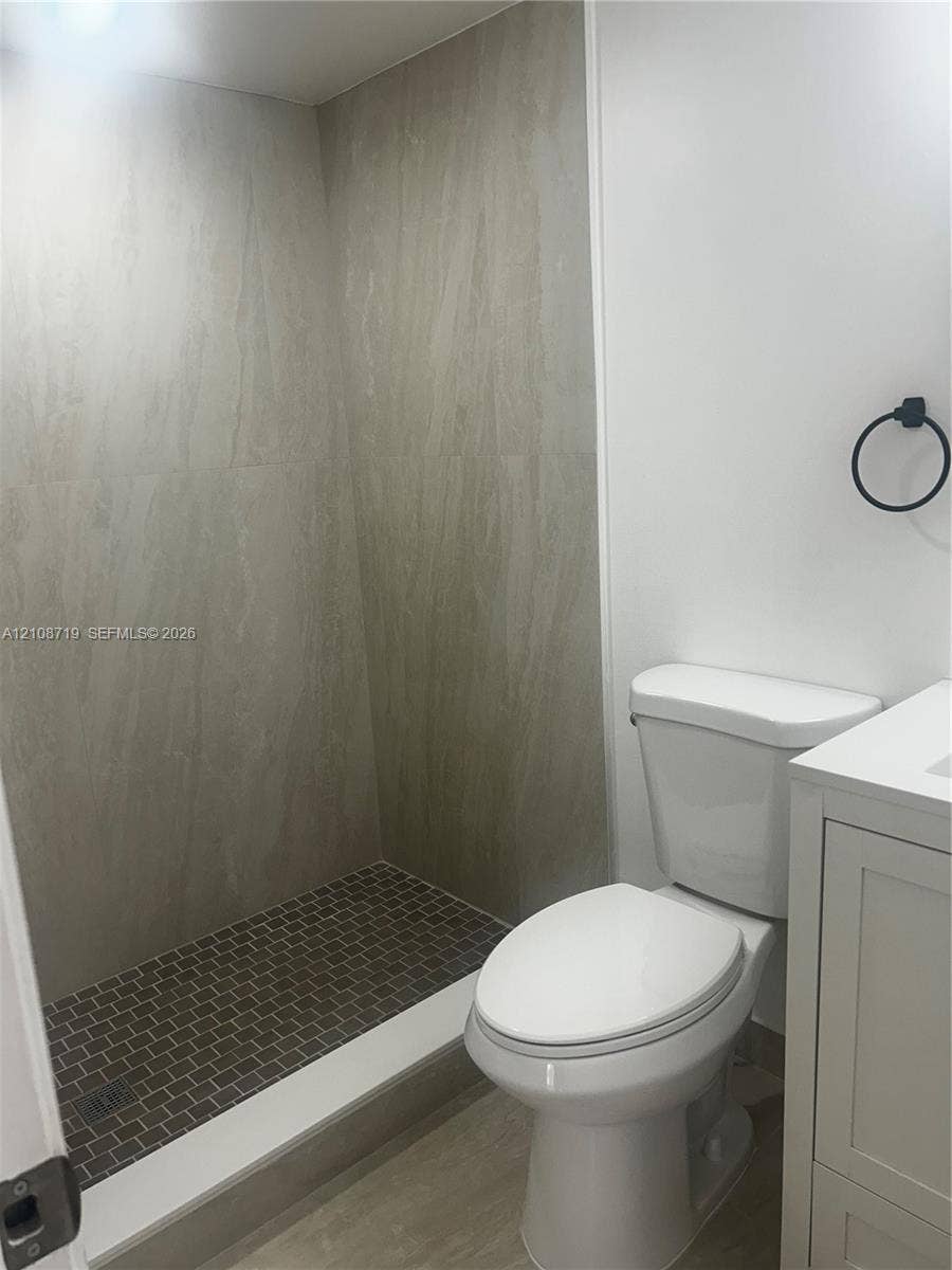 7035 NW 186th Street, #D309, Hialeah, Hialeah, FL 33015 Walk-in shower featuring large-format neutral wall tile, a mosaic tile floor, white vanity cabinet, and matte black hardware