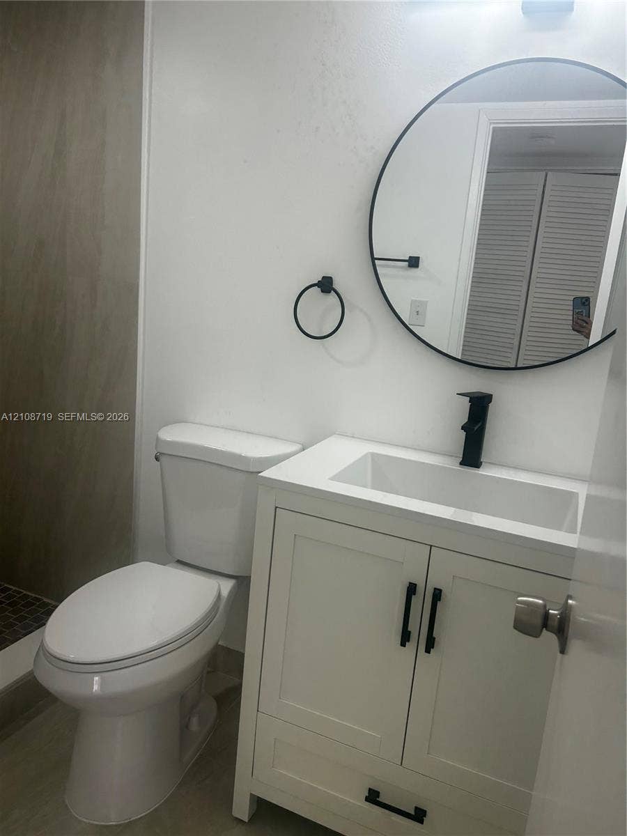 7035 NW 186th Street, #D309, Hialeah, Hialeah, FL 33015 White vanity cabinet featuring a rectangular basin, matte black faucet, and matching cabinet hardware, accented by a circular wall mirror and circular towel ring