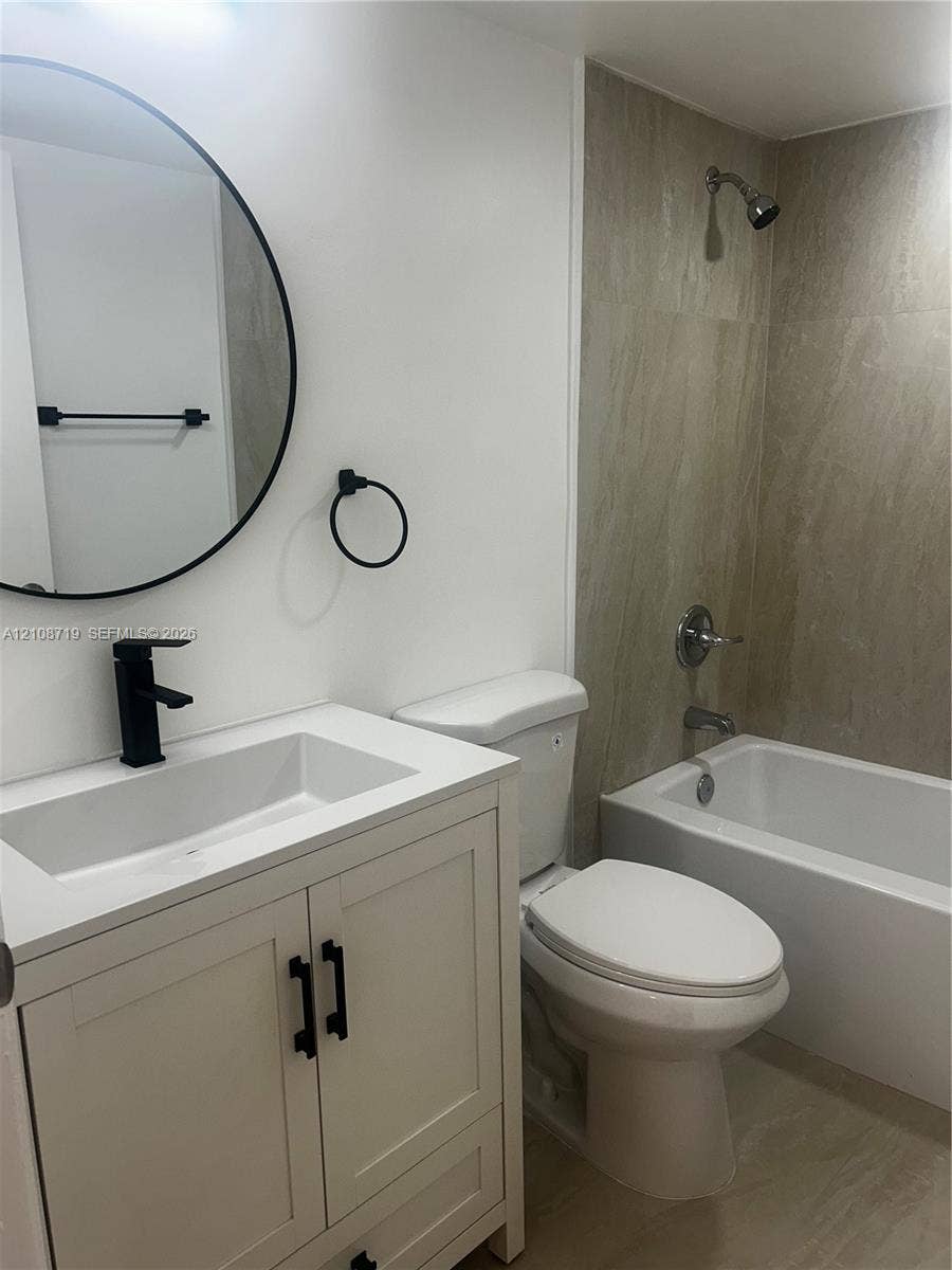 7035 NW 186th Street, #D309, Hialeah, Hialeah, FL 33015 Bathroom featuring a white vanity cabinet with a rectangular basin, matte black faucet, circular wall-mounted mirror, and tile-surround bathtub