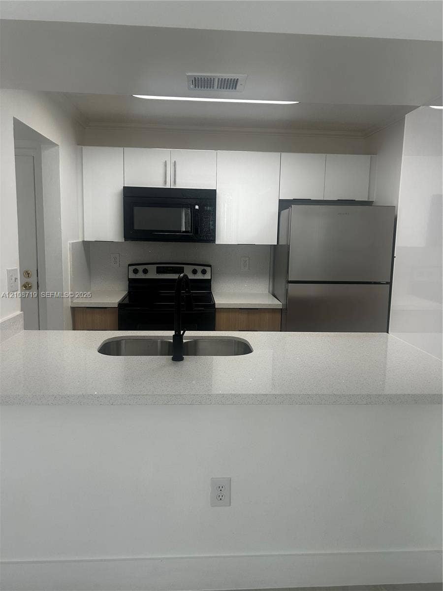 7035 NW 186th Street, #D309, Hialeah, Hialeah, FL 33015 Kitchen featuring white flat-panel cabinetry, quartz countertops, stainless steel appliances, and a dual-basin undermount sink with a matte black faucet