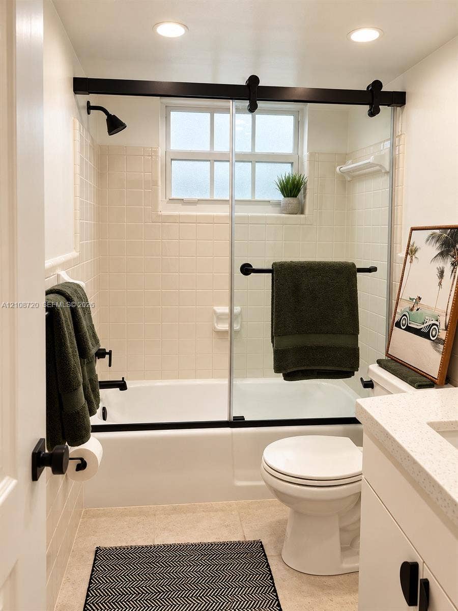 2404 NE 33rd Avenue, #3, Fort Lauderdale, FL 33305 Bathroom featuring a shower-tub combination, sliding glass door with matte black hardware, tile wall surround, and vanity with a light-toned countertop