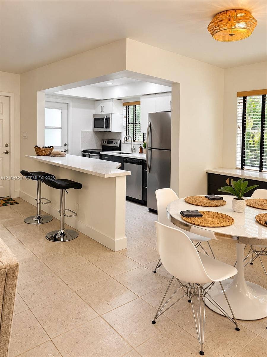 2404 NE 33rd Avenue, #3, Fort Lauderdale, FL 33305 Kitchen featuring a quartz breakfast bar, stainless steel appliances, white cabinetry, tile flooring, and a flush-mount drum light fixture
