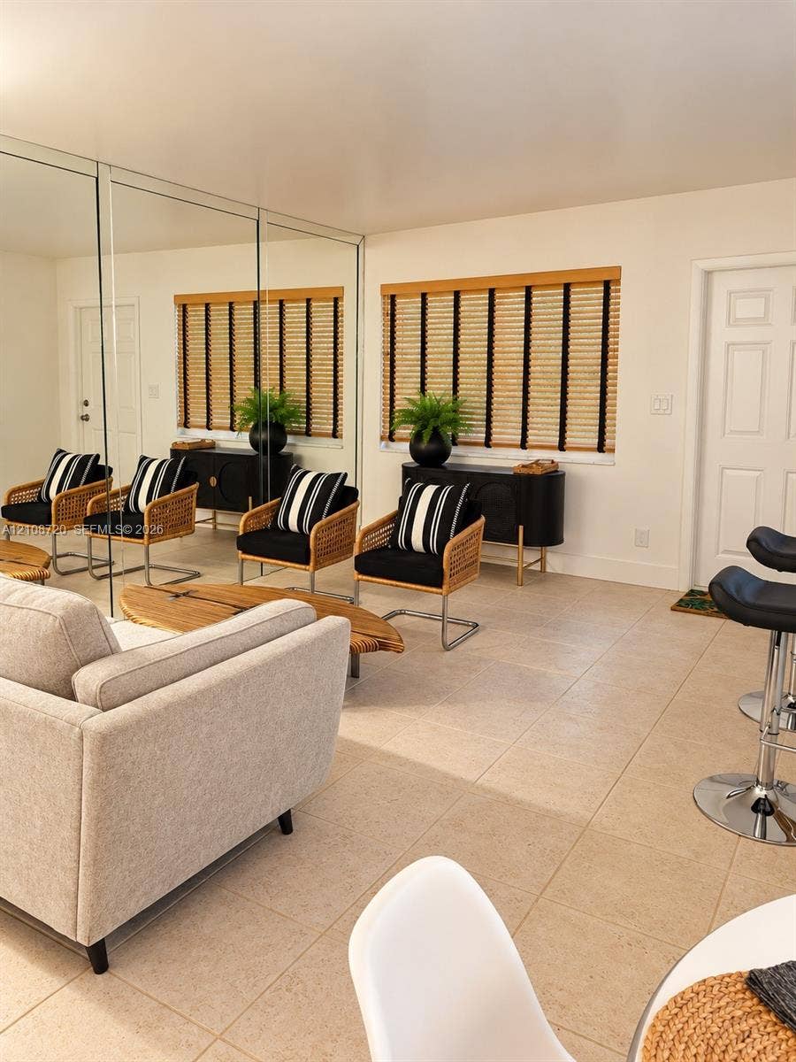 2404 NE 33rd Avenue, #3, Fort Lauderdale, FL 33305 Interior space featuring expansive wall-to-wall mirror panels, large-format tile flooring, and integrated window blinds with textured fabric detail