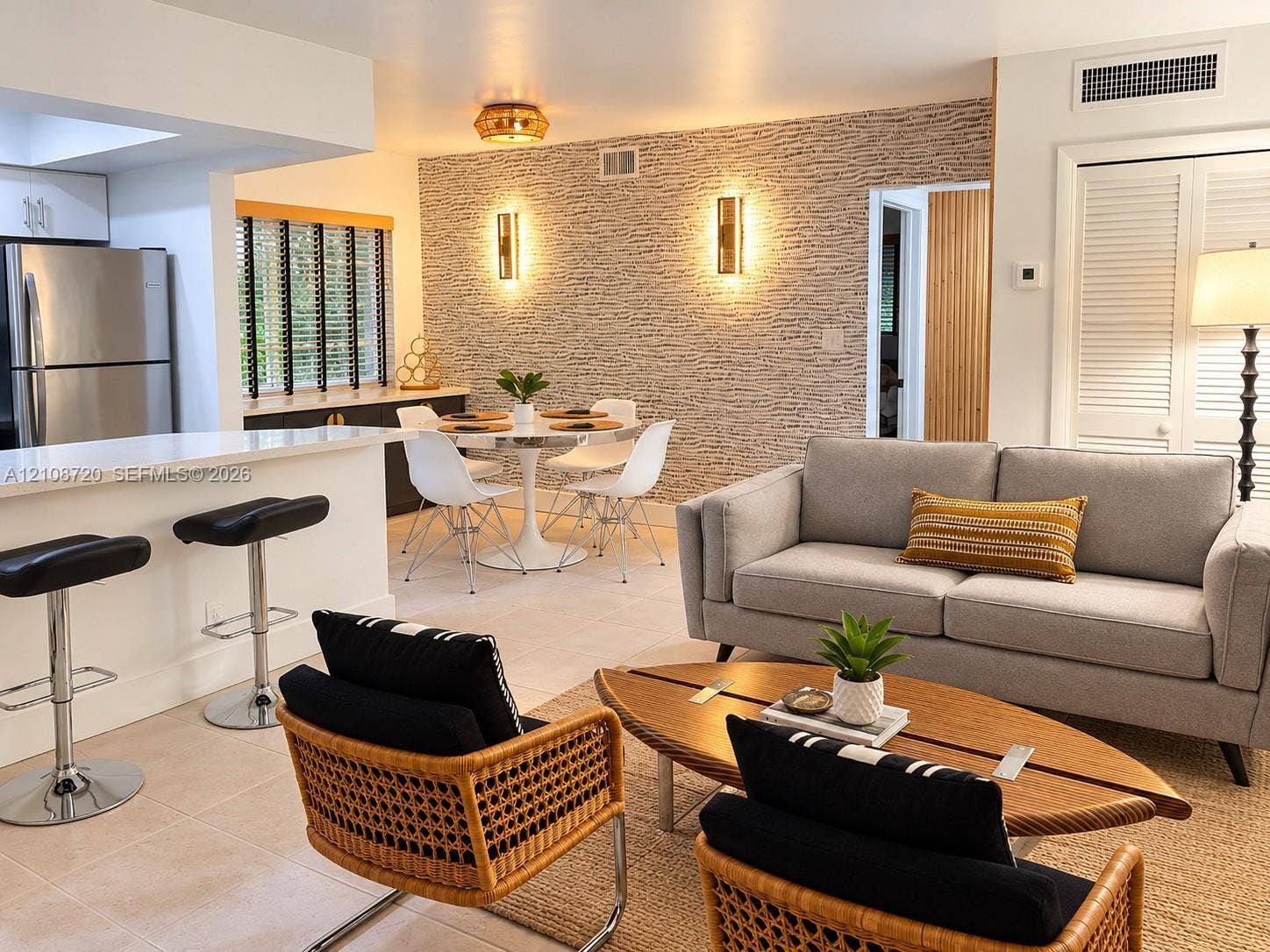 2404 NE 33rd Avenue, #3, Fort Lauderdale, FL 33305 Open-concept interior featuring textured stone-look accent wall, dual vertical wall-mounted sconces, breakfast bar with integrated cabinetry, tile flooring, and louvered closet doors