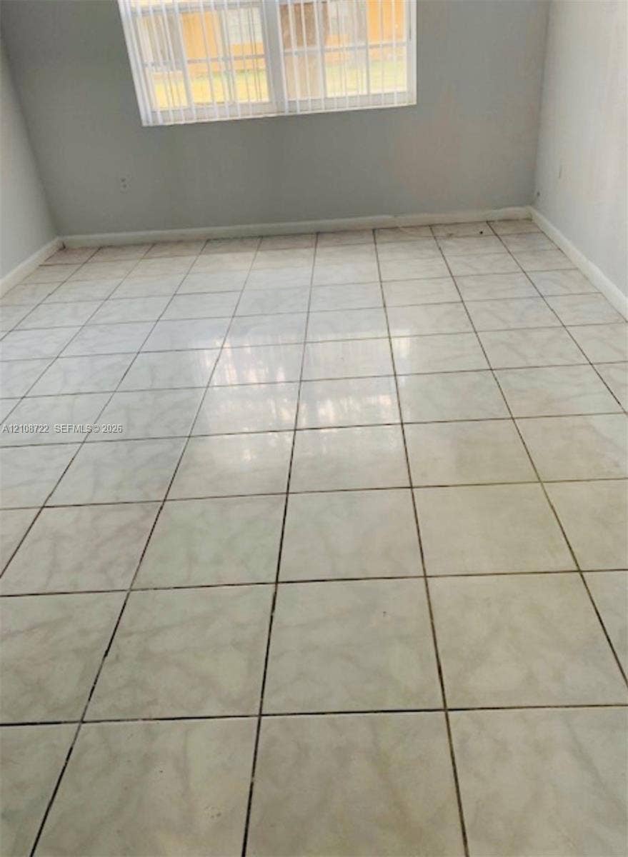 505 NW 177th Street, #110, Miami Gardens, Miami Gardens, FL 33169 Neutral-toned interior space featuring large-format ceramic tile flooring, light grey wall paint, and a double-hung window with installed vertical blinds