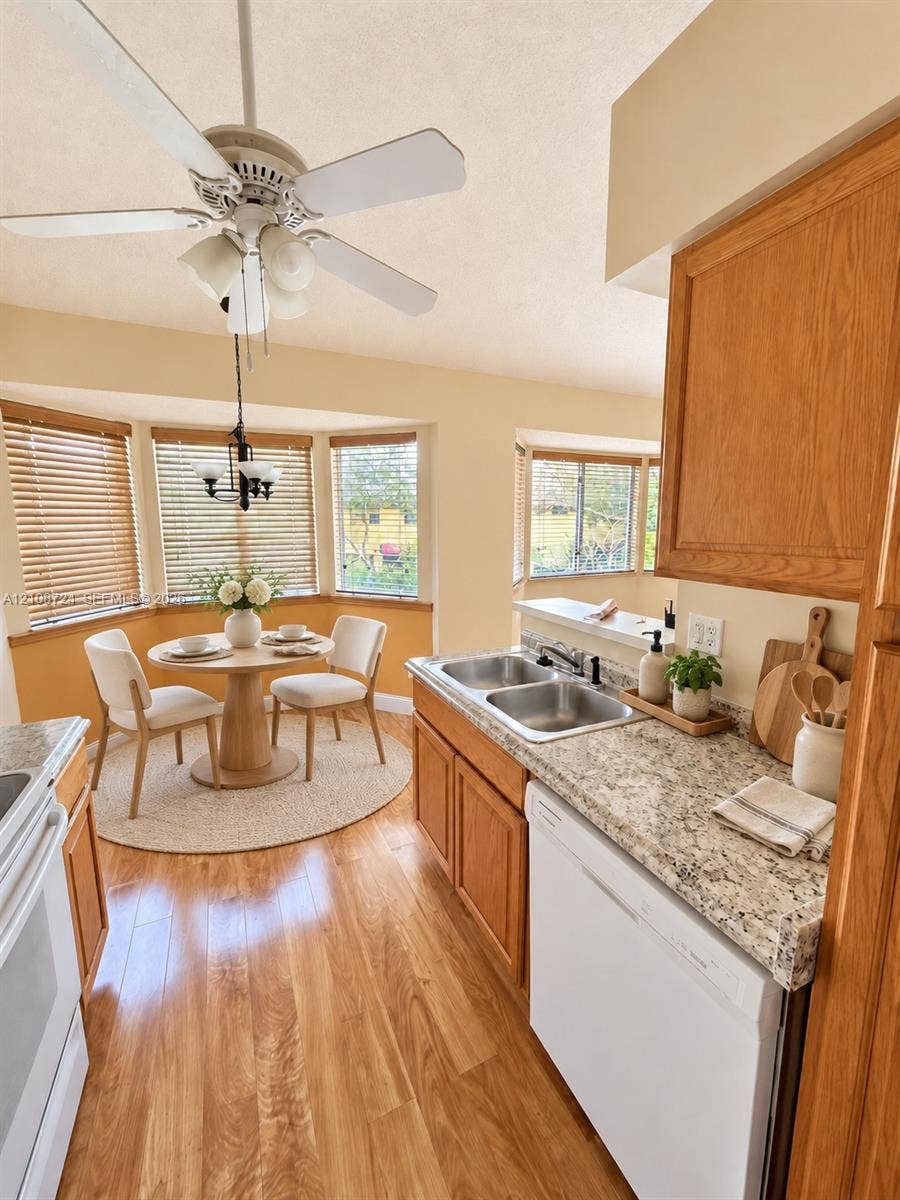 972 NW 92nd Terrace, Plantation, Plantation, FL 33324 Kitchen featuring wood-finish cabinetry, stone-texture countertops, a dual-basin stainless steel sink, wood-finish flooring, and a bay window breakfast nook