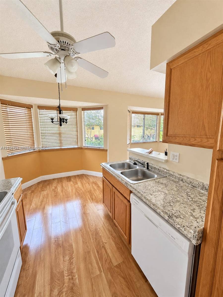 972 NW 92nd Terrace, Plantation, Plantation, FL 33324 Kitchen featuring wood-finish flooring, stone-patterned countertops, a dual-basin stainless steel sink, wood cabinetry, and bay windows