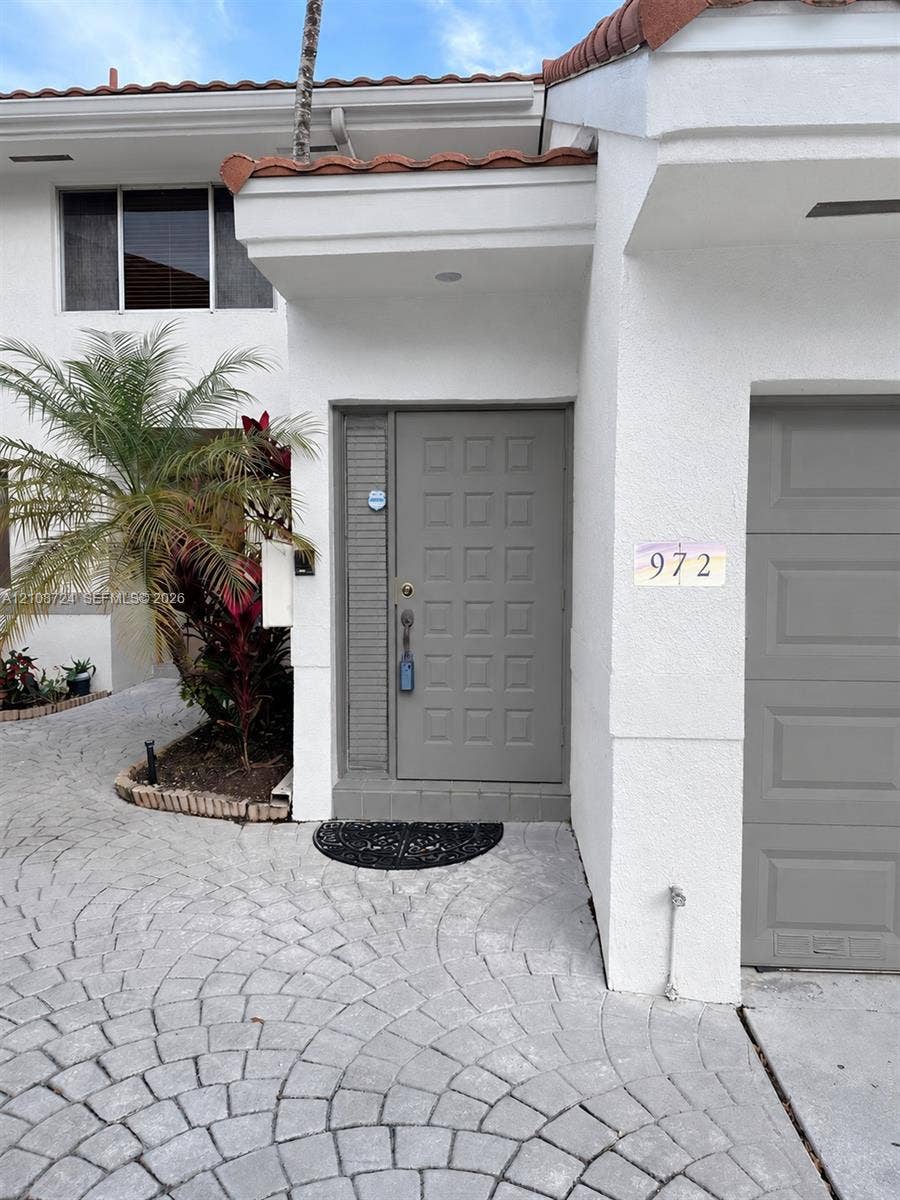 972 NW 92nd Terrace, Plantation, Plantation, FL 33324 Stucco exterior featuring a tiled roof, gray paneled front door, and a patterned stone-paver driveway