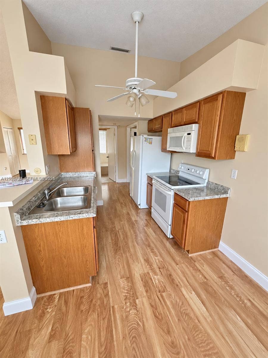 972 NW 92nd Terrace, Plantation, Plantation, FL 33324 Kitchen featuring wood-finish cabinetry, stone-style countertops, stainless steel dual-basin sink, wood-finish flooring, and ceiling-mounted light fixture with fan