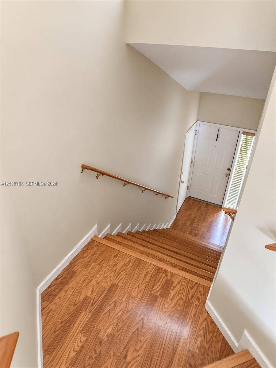 972 NW 92nd Terrace, Plantation, Plantation, FL 33324 Staircase featuring wood-finish flooring, a wall-mounted wooden handrail, and an entry door with a side window panel