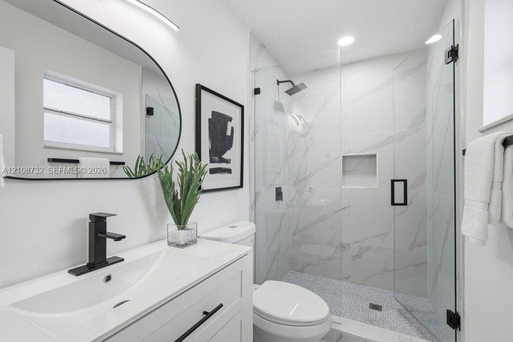 Modern vanity with a rectangular sink, matte black faucet, and curved mirror, complemented by a walk-in shower featuring large-format stone-look wall tiles, a built-in recessed niche, and a glass enclosure with matte black hardware