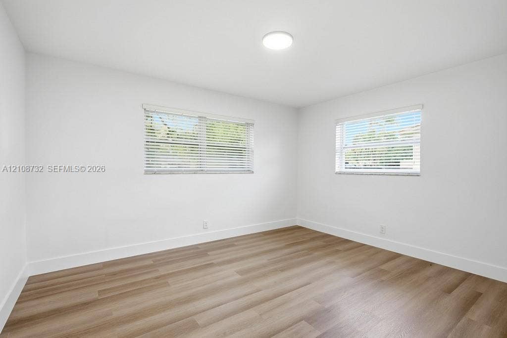 Interior room featuring wood-finish flooring, two dual-pane windows with horizontal blinds, and a circular flush-mount ceiling light