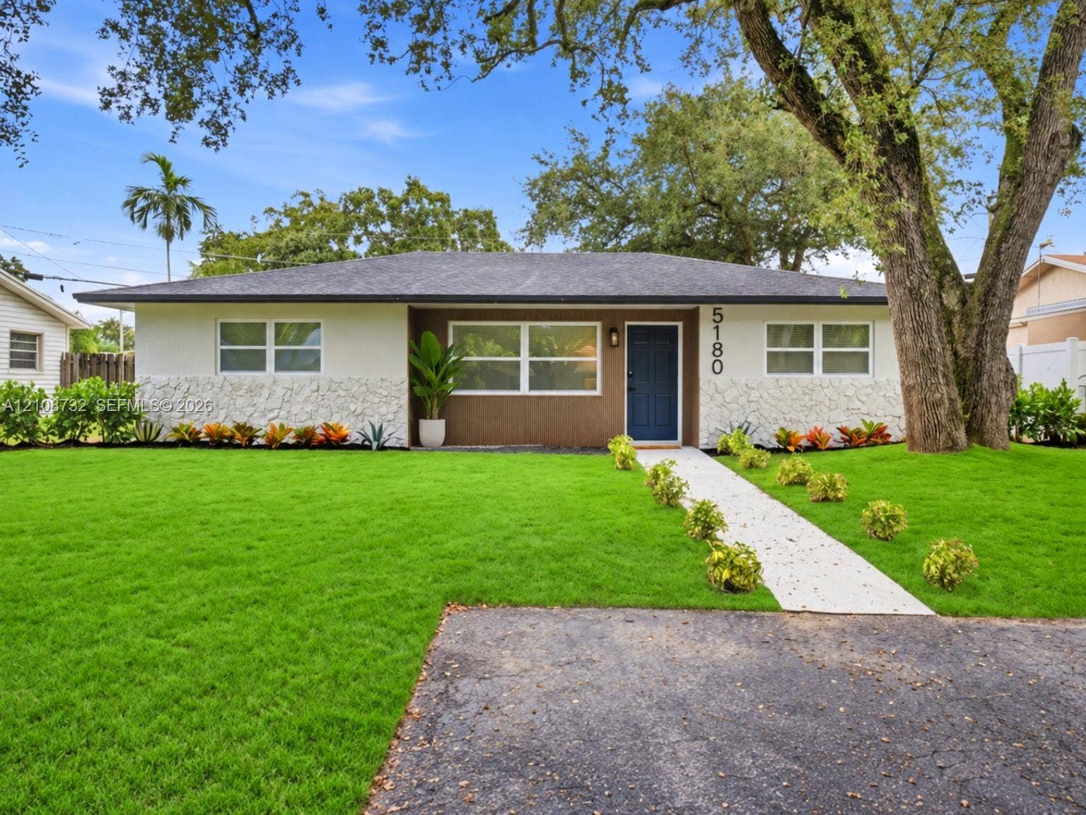 Single-story exterior featuring light-toned textured stone accents, a deep-toned shingled roof, a central entry with a paneled door, and a concrete walkway