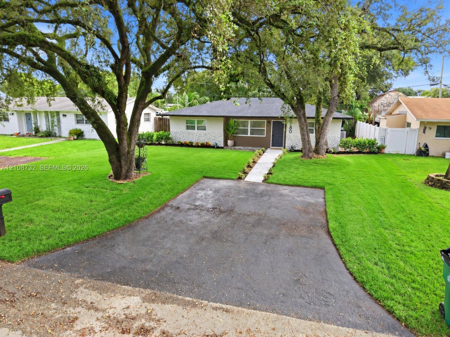 Single-story exterior featuring a stone veneer facade, asphalt driveway, concrete paver walkway, and mature trees