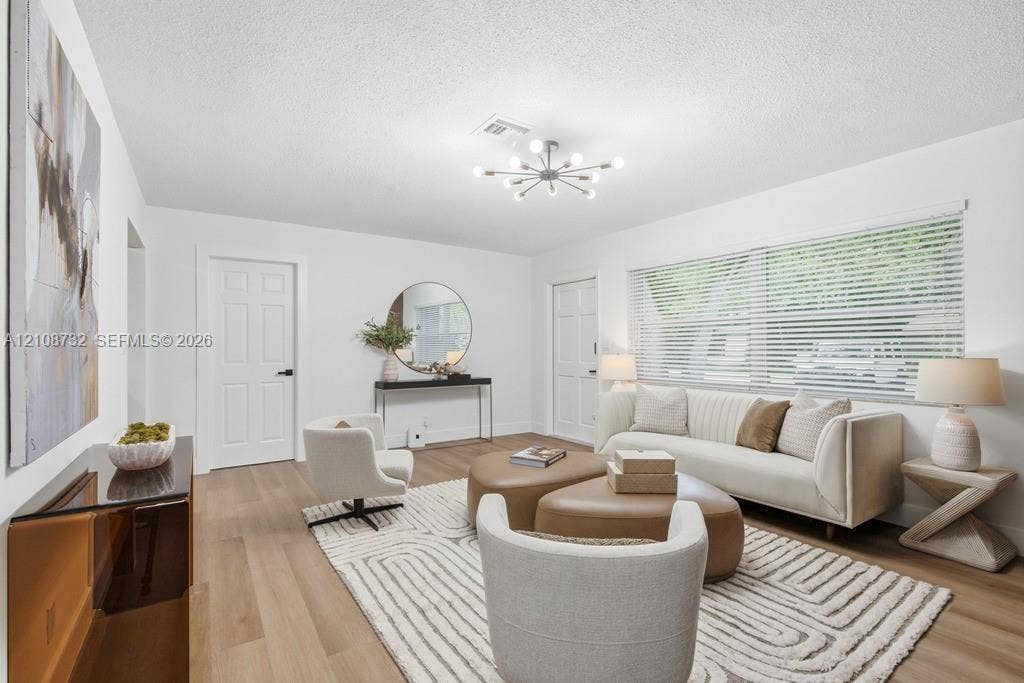 Living area featuring wood-finish flooring, a modern multi-arm sputnik chandelier, and a large window with horizontal blinds