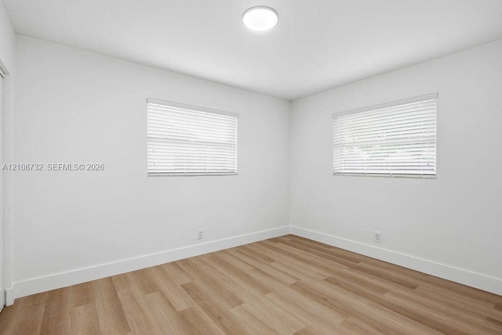 Neutral interior room featuring wood-finish flooring, two windows with horizontal blinds, and a central flush-mount ceiling light fixture