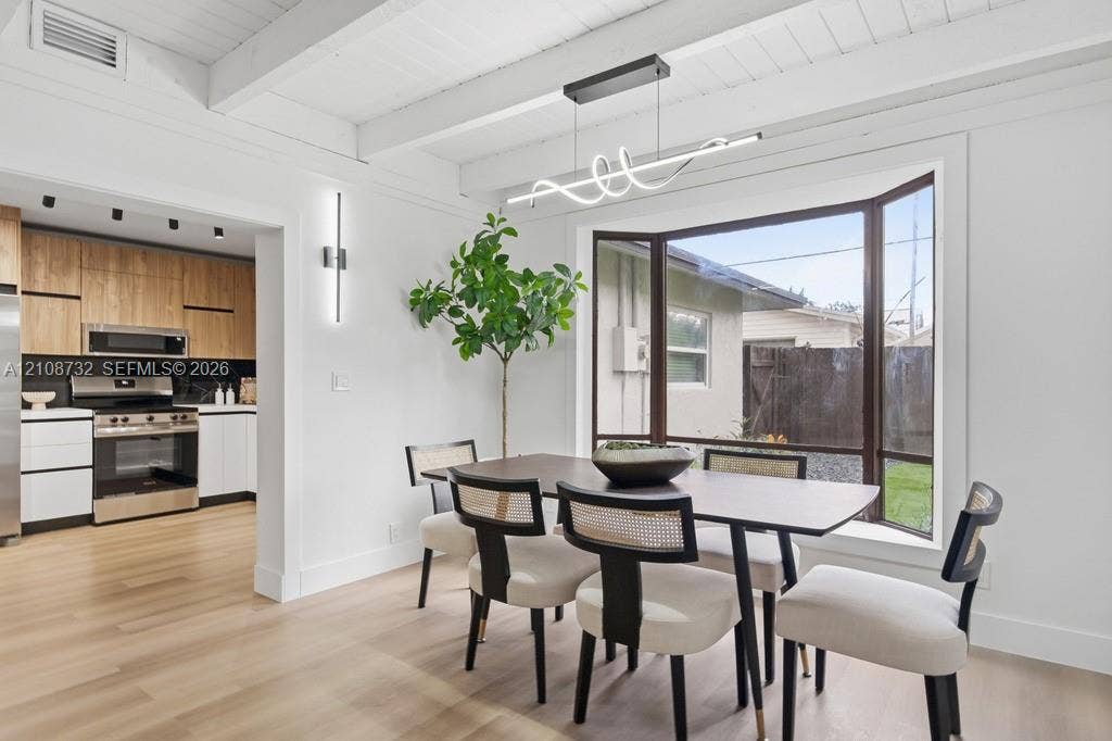 Exposed beam ceiling, light wood-finish flooring, bay window, contemporary linear LED chandelier, and modern wall-mounted accent lighting