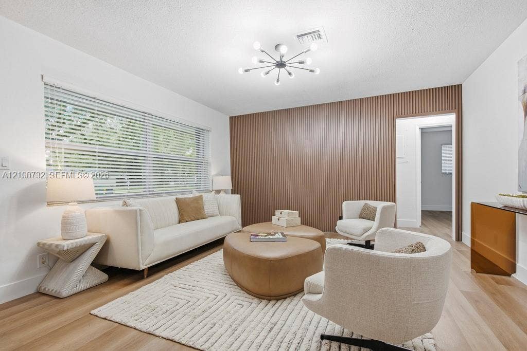 Living space featuring wood-finish flooring, a decorative vertical-slat accent wall, and a multi-bulb sputnik-style light fixture