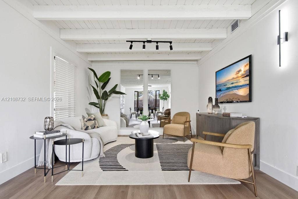 Living area featuring exposed beam ceilings, wood-finish flooring, adjustable track lighting, and a linear wall-mounted light fixture