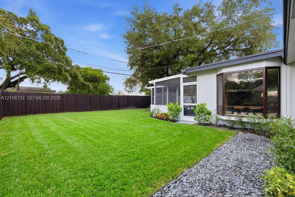 Backyard featuring a manicured lawn, enclosed porch, bay window, perimeter privacy fencing, and decorative stone landscaping