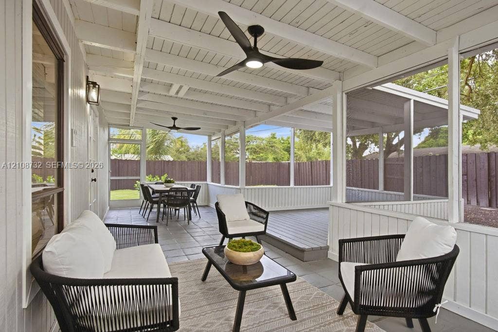 Screened-in porch featuring a painted wood-beamed ceiling, tile flooring, built-in ceiling fans, and a raised wooden deck platform