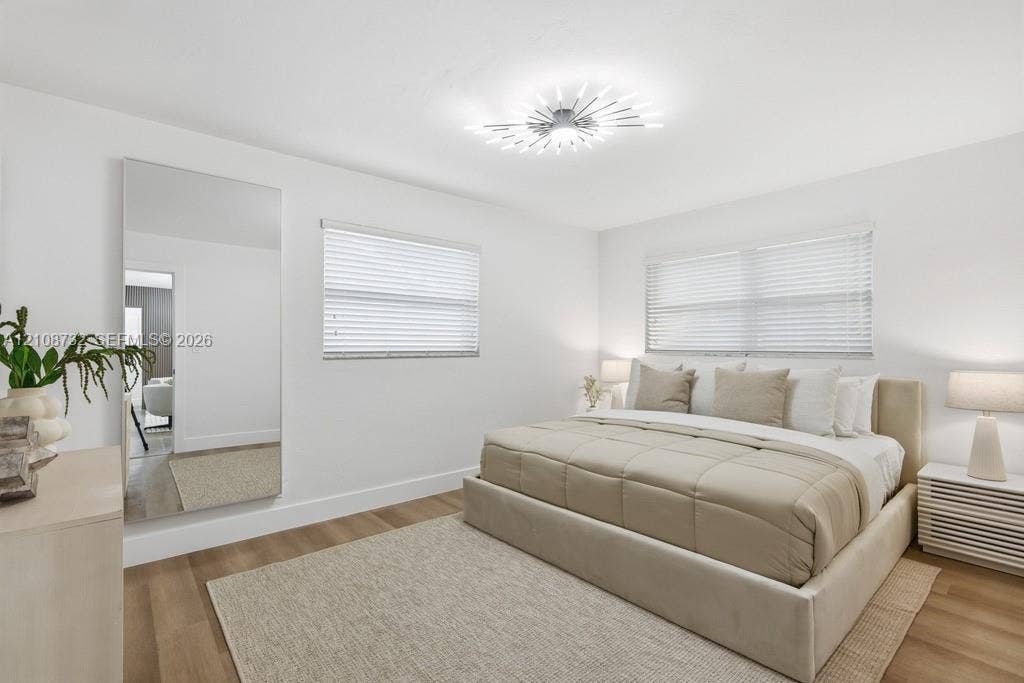 Neutral-toned interior featuring wood-finish flooring, full-length wall mirror, horizontal window blinds, and a contemporary sunburst-style flush mount ceiling light fixture