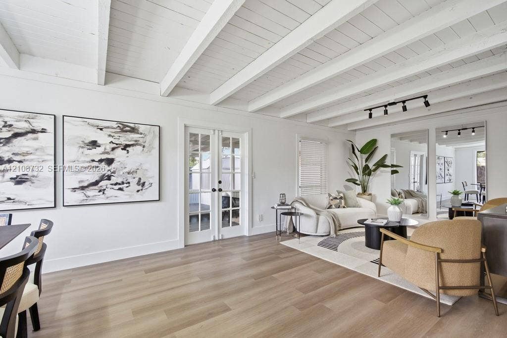 Vaulted ceilings featuring exposed white-painted beams, light wood-finish flooring, glass-paned French doors, and ceiling-mounted track lighting