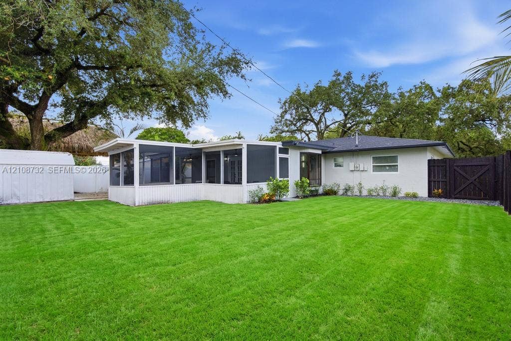 Expansive backyard featuring a manicured lawn, screened-in porch, mature shade trees, and a wooden privacy fence