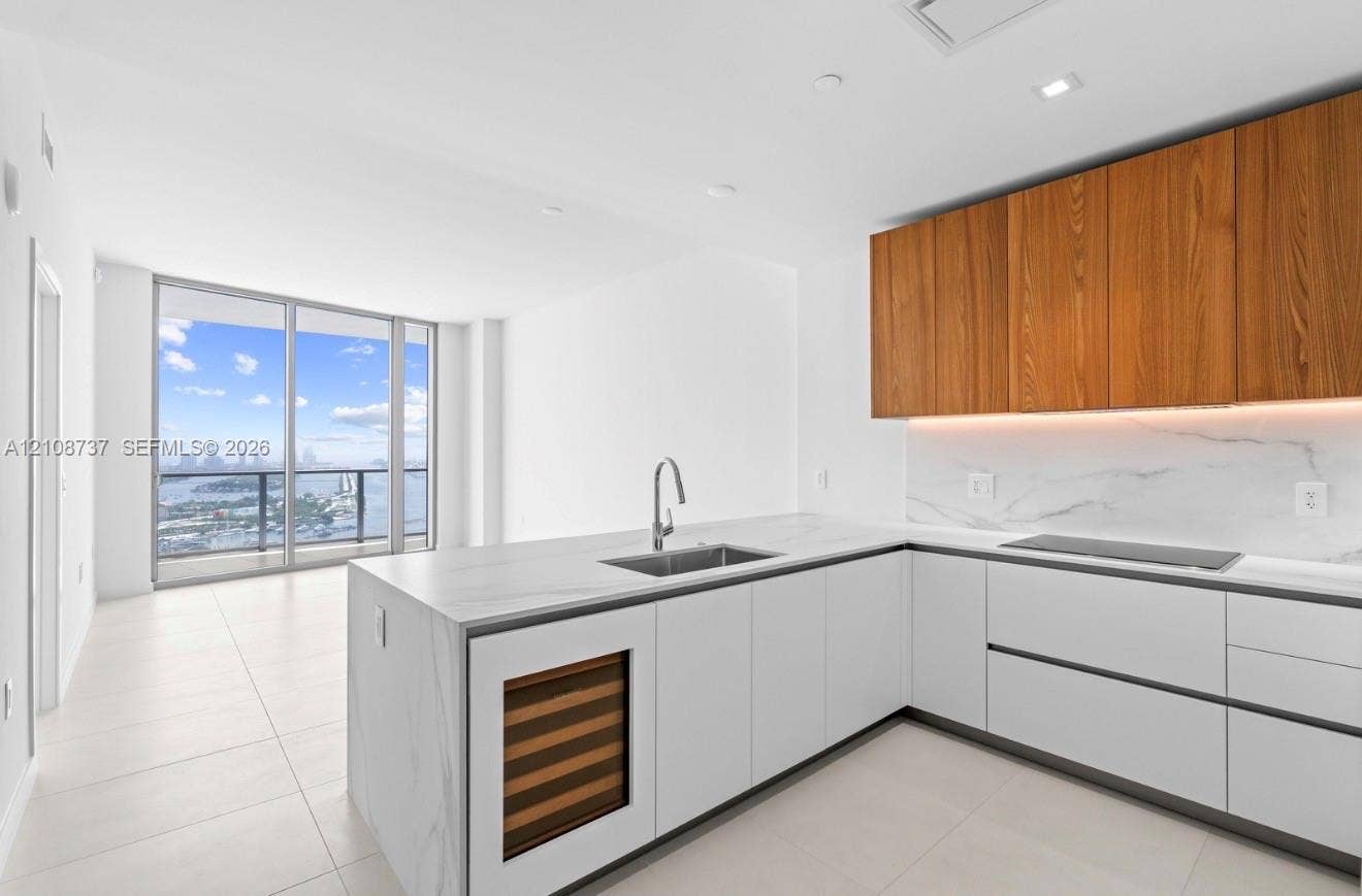 1400 Biscayne Boulevard, #3503, Miami, Miami, FL 33132 Modern kitchen featuring stone-surfaced countertops, custom wood-finish cabinetry, built-in wine refrigeration, integrated cooktop, and floor-to-ceiling windows
