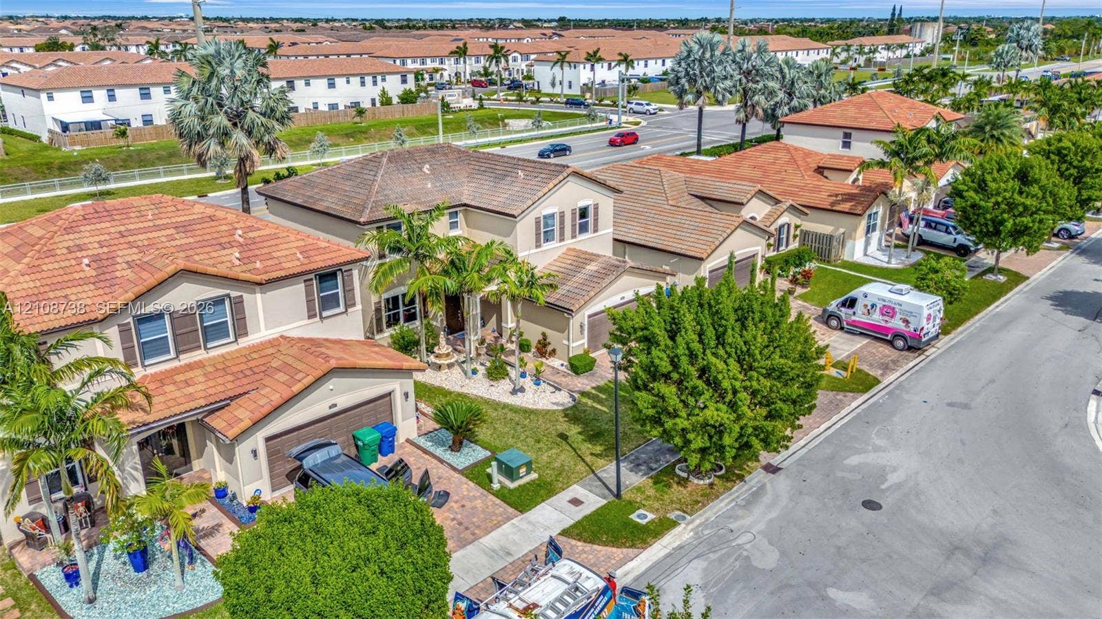 Two-story residence featuring a clay tile roof, paved driveway, multi-car garage, and mature palm landscaping