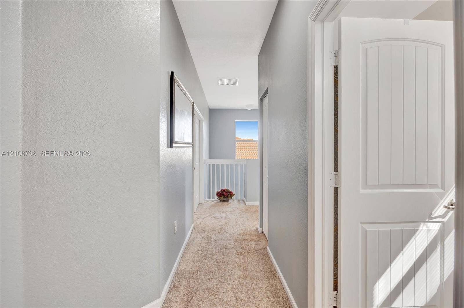 Hallway featuring neutral-toned carpeting, two-panel interior doors, light-colored wall paint, and a decorative railing