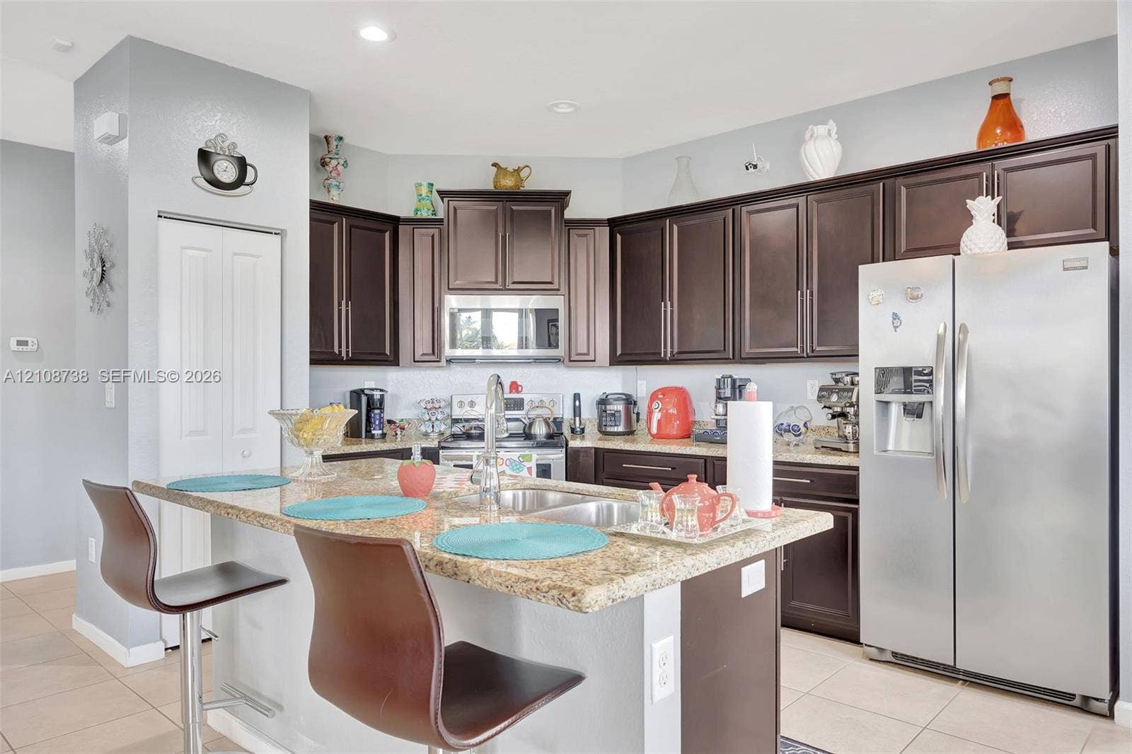 Kitchen featuring dark wood cabinetry, stone countertops, stainless steel appliances, a central island with a double-basin sink, and recessed ceiling lighting