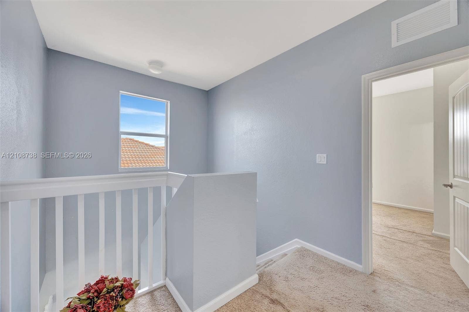 Neutral-toned interior featuring white baluster railing, wall-to-wall carpeting, and a multi-panel door
