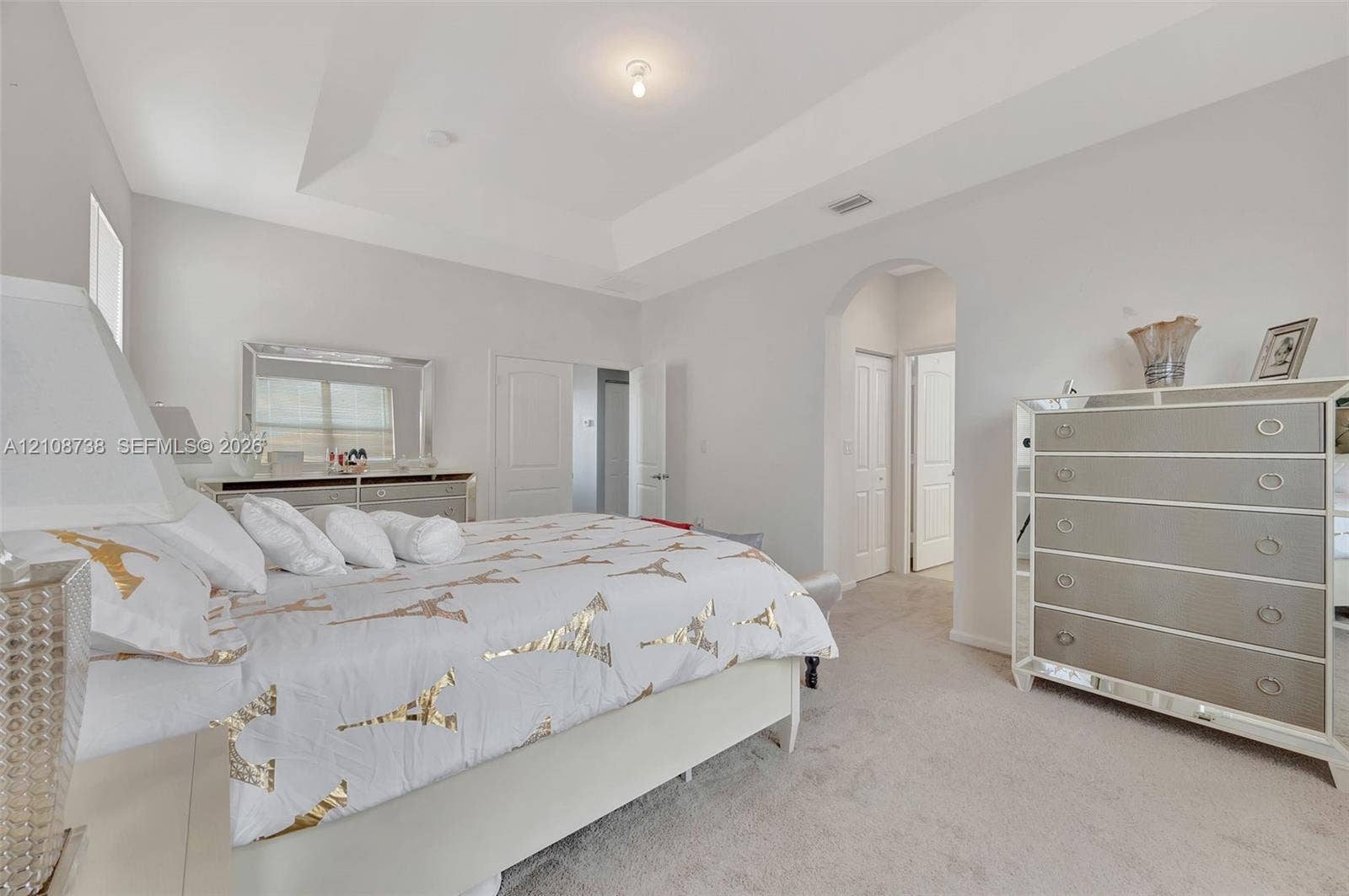 Tray ceiling, neutral wall tones, arched entryway, and neutral carpeted flooring