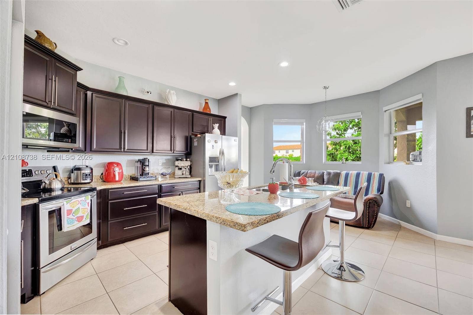Kitchen featuring dark cabinetry, stone-surface countertops, stainless steel appliances, a center island with a breakfast bar, and tile flooring