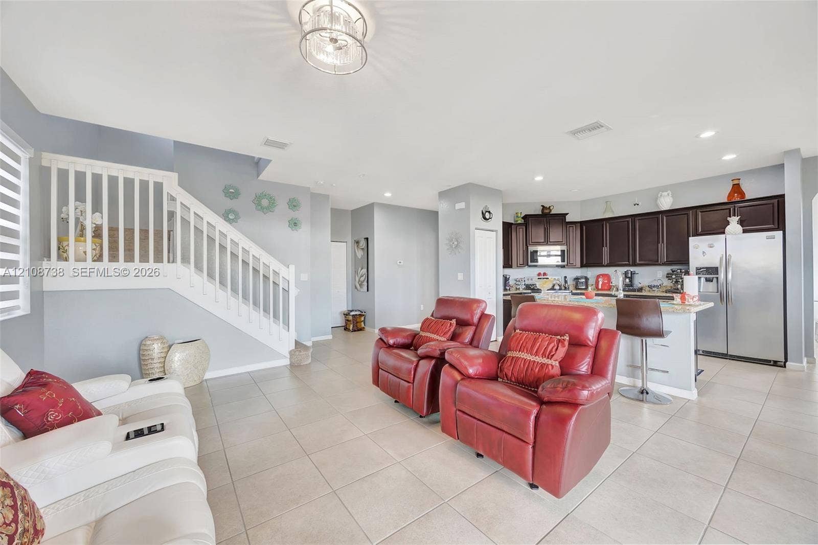 Open-concept interior featuring tile flooring, a white staircase with a vertical baluster railing, dark-toned cabinetry, stainless steel kitchen appliances, and recessed lighting