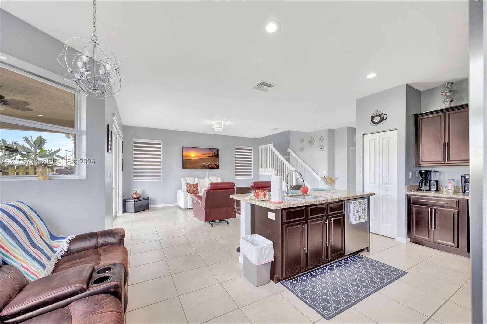 Open-concept interior featuring large-format tile flooring, a kitchen island with stone surfacing, espresso-toned cabinetry, recessed lighting, and a modern sculptural pendant fixture