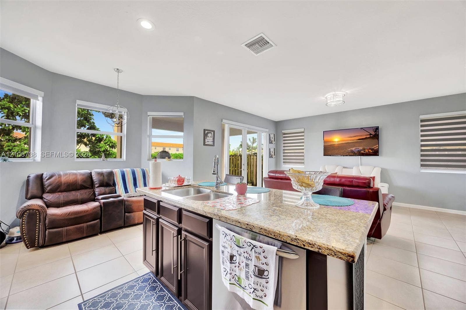Kitchen island featuring a stone countertop, dual-basin stainless steel sink, and dark-toned cabinetry, complemented by tile flooring and recessed lighting