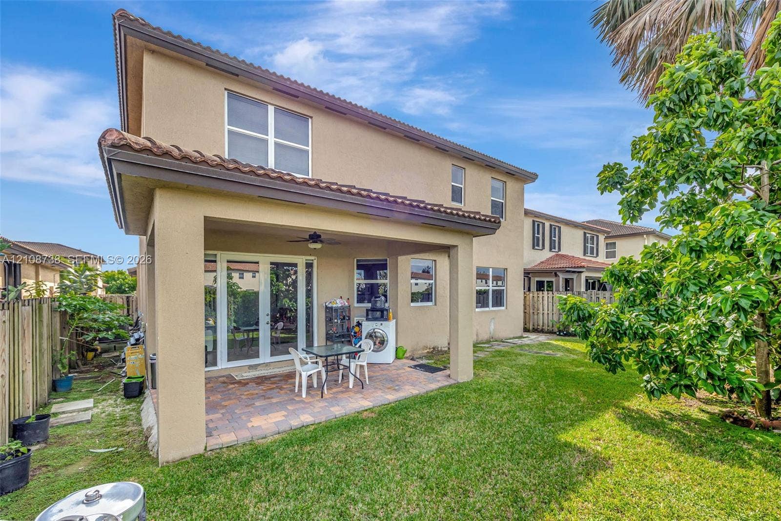 Stucco exterior with a tiled roof, featuring a covered patio with paver flooring, a built-in ceiling fan, and glass French doors