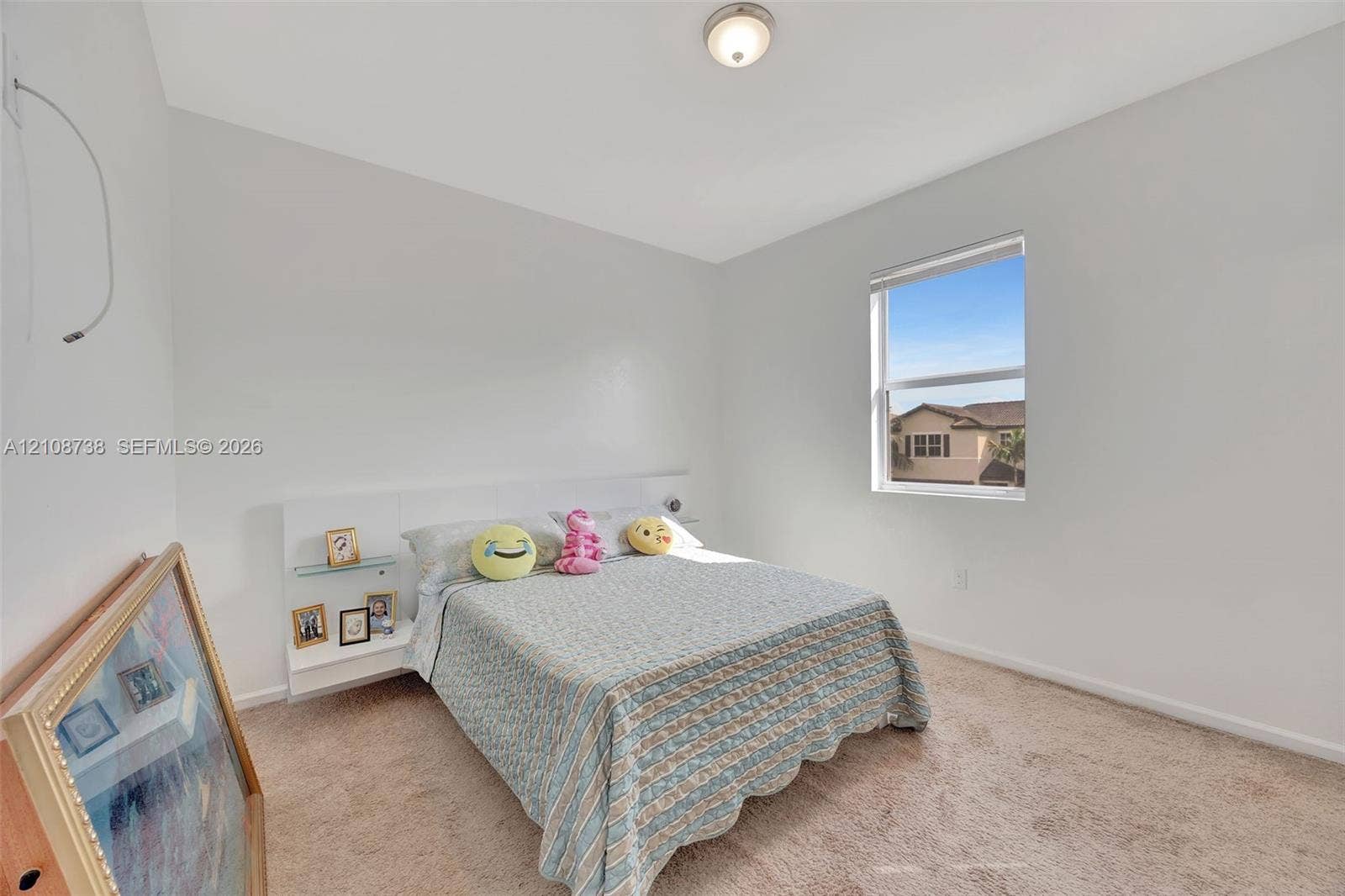 Neutral-toned walls, high ceilings, carpeted flooring, built-in headboard with integrated shelving, and a single-pane window