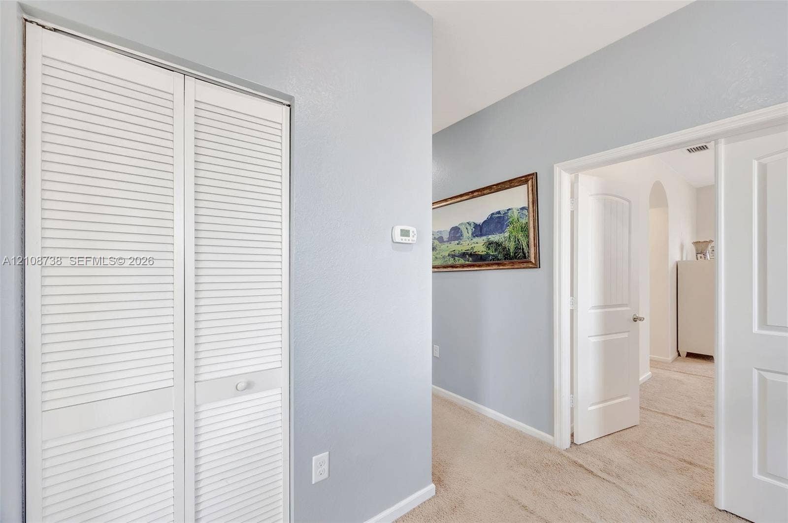 Interior hallway featuring white louvered-style bi-fold doors, neutral wall paint, and arched doorway entry