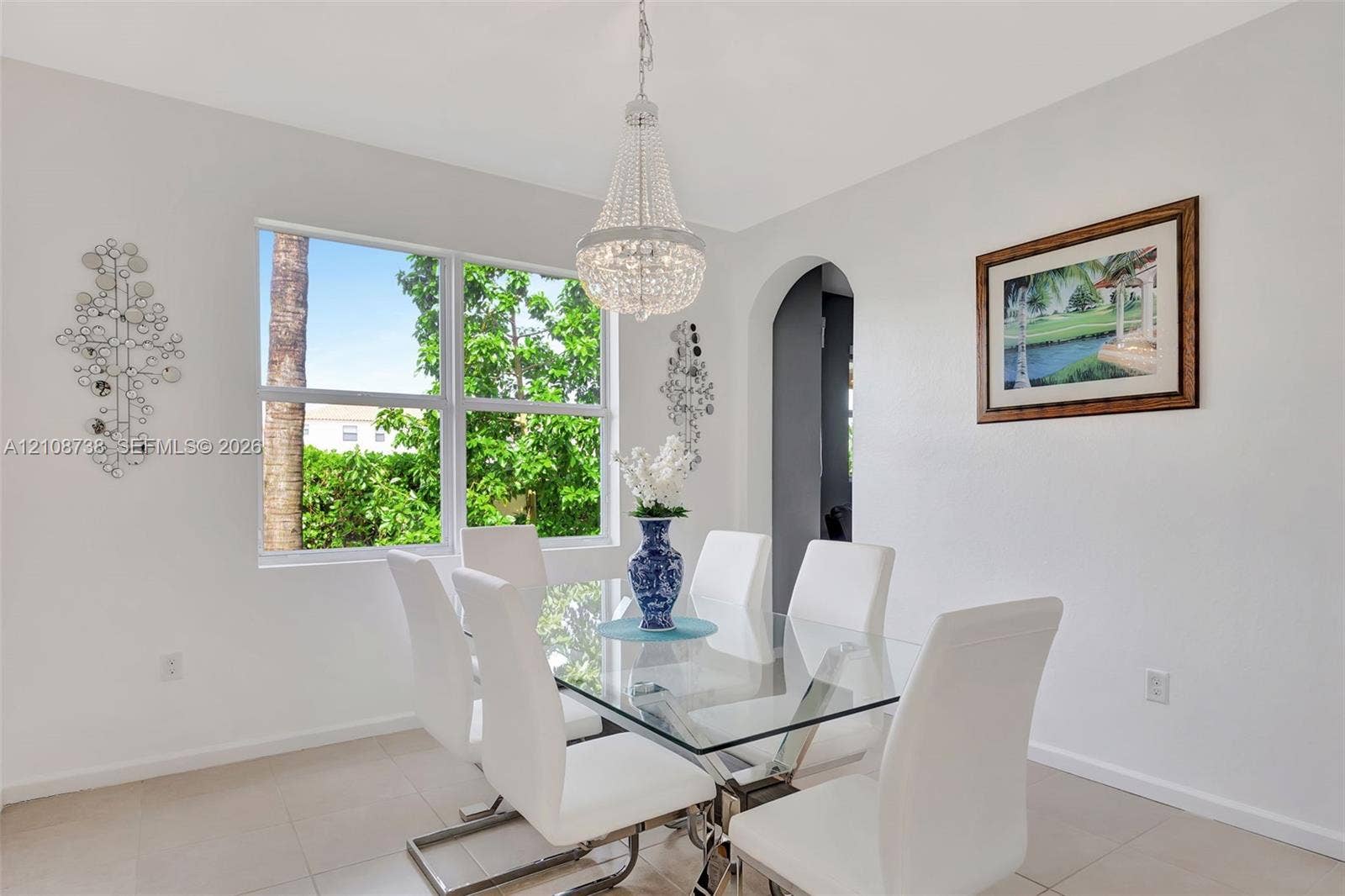 Dining area featuring large-format tile flooring, a crystal tiered chandelier, a picture window, and an arched entryway