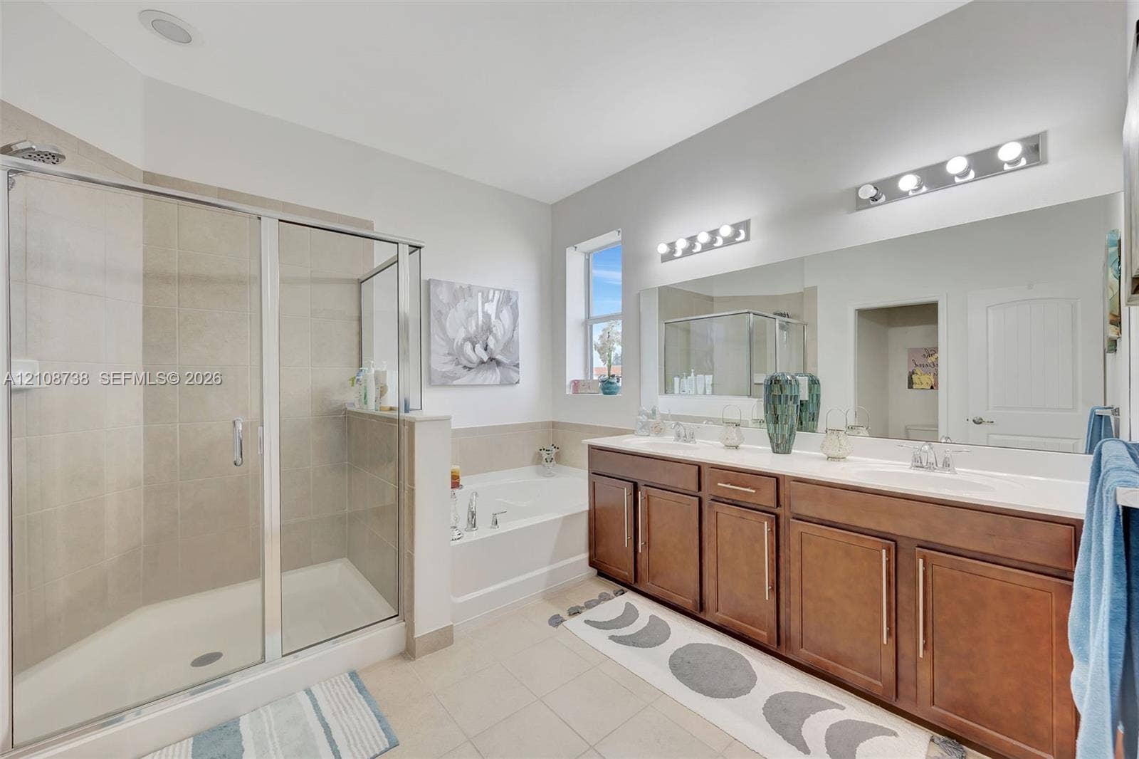 Bathroom featuring a walk-in shower with glass enclosure, soaking tub, dual-sink vanity with wood cabinetry, and large-format wall-to-wall mirror