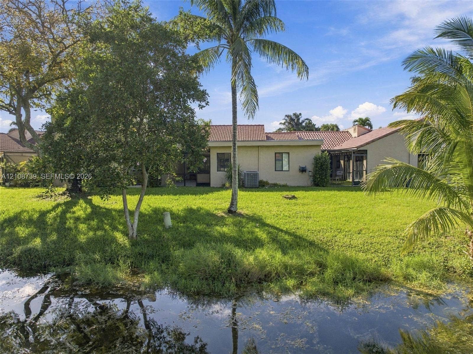 632 Village Lake Drive, Weston, FL 33326 Backyard featuring a waterfront location, expansive lawn, mature palm trees, and a tile roof