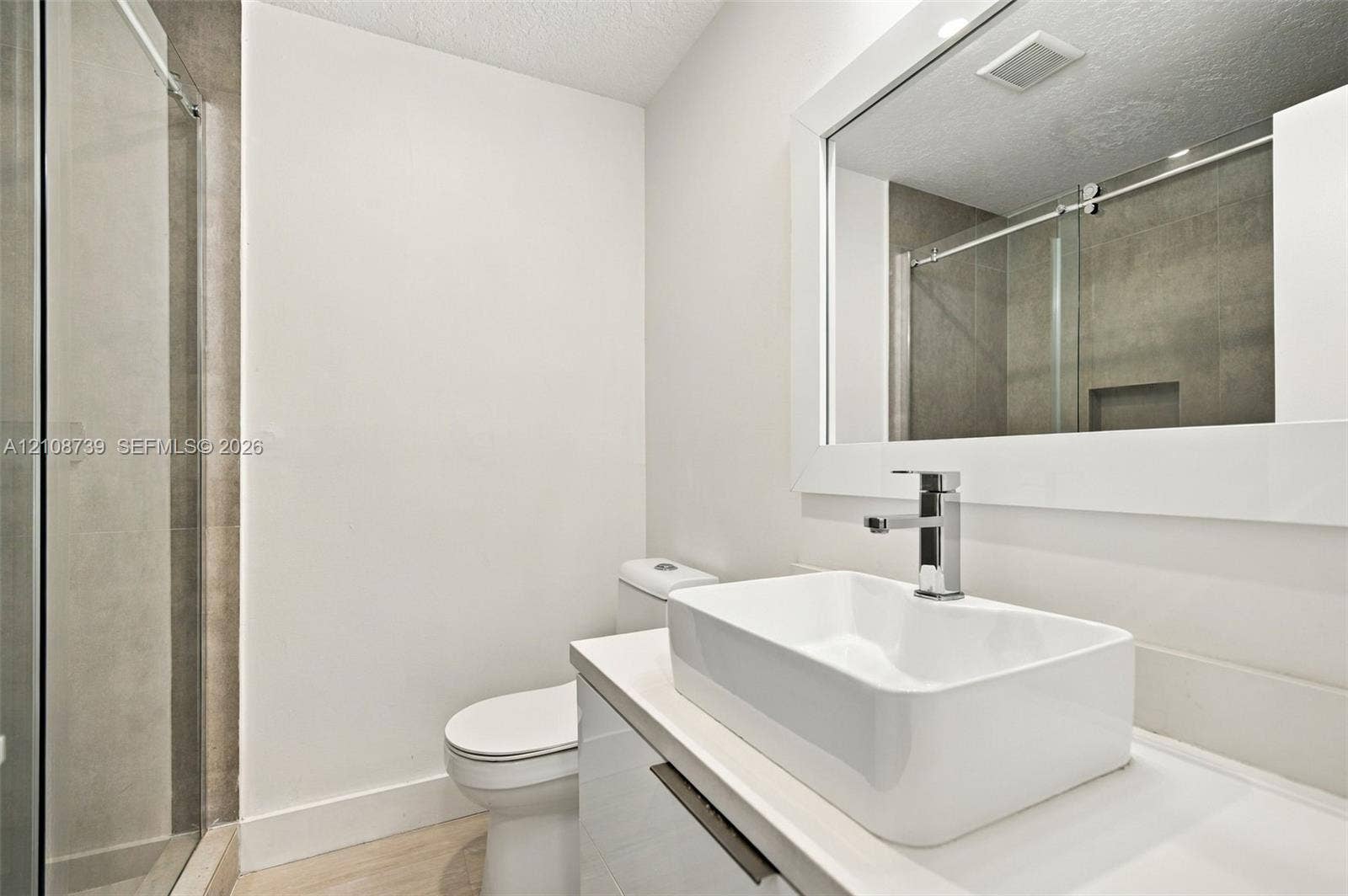 632 Village Lake Drive, Weston, FL 33326 Bathroom featuring a rectangular vessel sink, wall-mounted mirror with a white frame, gloss-finish vanity, glass-enclosed shower, and polished chrome fixtures