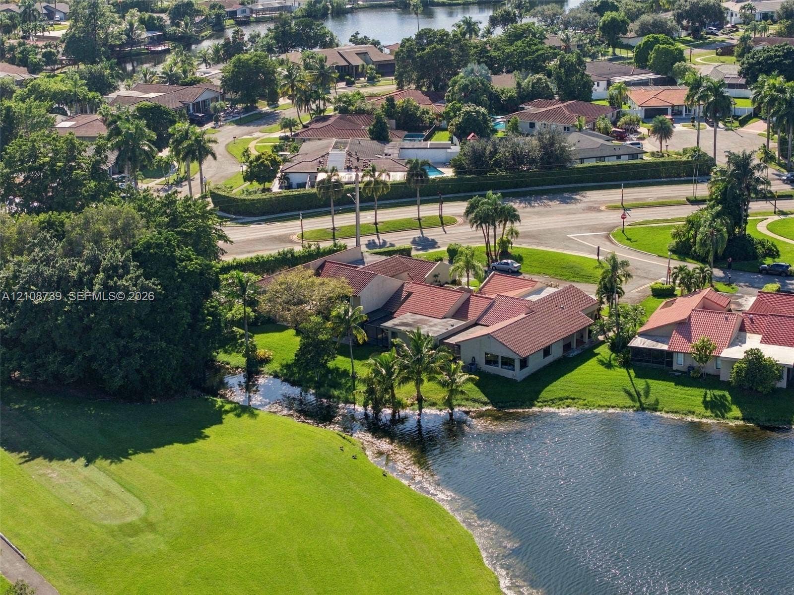 632 Village Lake Drive, Weston, FL 33326 Waterfront property featuring a tile roof, mature palms, expansive lawn, and direct proximity to a golf course